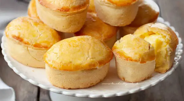 Un mucchio di pasticciotti pugliesi dorati e invitanti su un alzatina bianca.