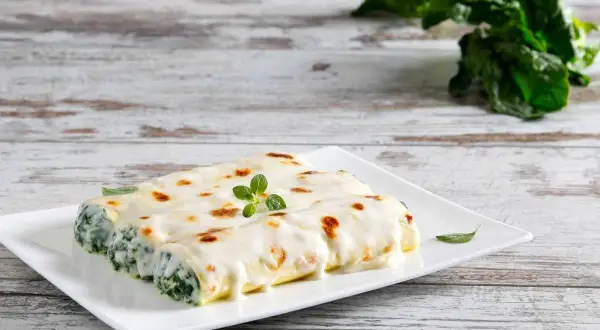 Cannelloni ricotta e spinaci gratinati, serviti su un piatto bianco con una guarnizione di origano fresco.