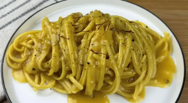 Un piatto di pasta alla milanese cremosa, con fili di zafferano e pepe nero.