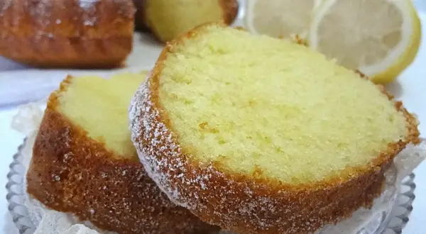Fette di ciambellone al limone spolverate di zucchero a velo, con limoni freschi sullo sfondo.