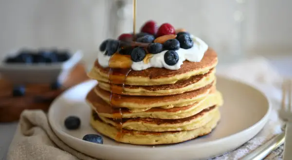 Pancake con yogurt, mirtilli, lamponi e sciroppo d'acero che cola. Un dolce inizio di giornata.