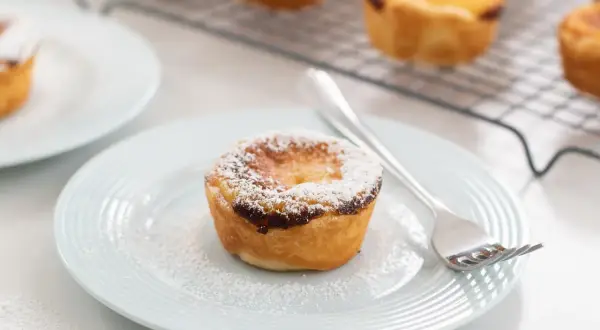Un delizioso pastel de nata, cosparso di zucchero a velo, su un piatto azzurro con una forchetta.