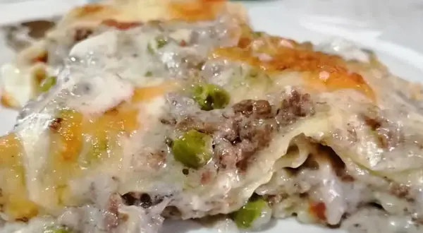 Porzione di lasagna bianca con ragù, piselli e besciamella filante, gratinata al forno.