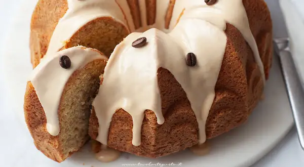 Una deliziosa torta al caffè, con glassa chiara e chicchi di caffè come decorazione. Una fetta è stata tagliata, rivelando l'interno soffice.