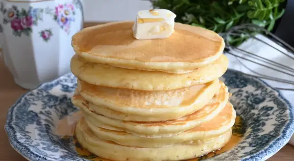 Pancake con farina di avena, una pila dorata con burro e sciroppo, serviti su un piatto decorato.