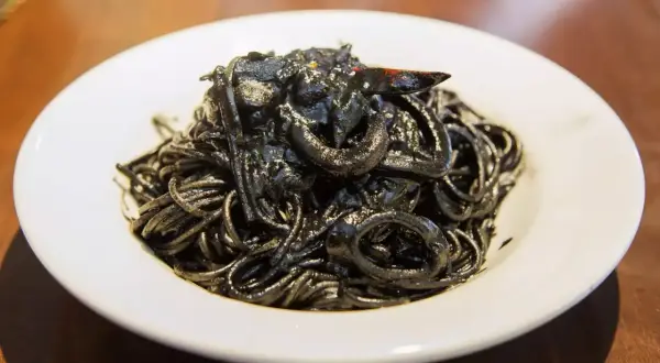 Un piatto invitante di spaghetti al nero di seppia, con anelli di calamaro e un peperoncino.