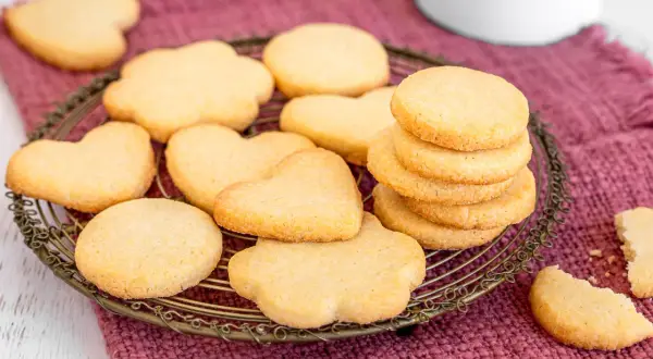 Deliziosi dolci per colazione a forma di cuore e fiore, serviti su un cestino di metallo dorato, su un tovagliolo di stoffa color prugna.