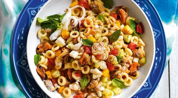 Deliziosa insalata di pasta con cozze, calamari, gamberi, pomodorini e basilico fresco. Un piatto estivo perfetto.