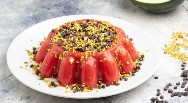 Delizioso gelo di anguria, guarnito con gocce di cioccolato e pistacchi tritati, su un piatto bianco.