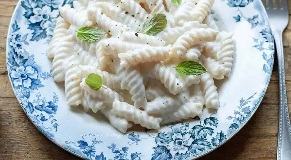 Fusilli cremosi conditi con una salsa vellutata alla ricotta, guarniti con foglie di menta fresca su un piatto decorato.