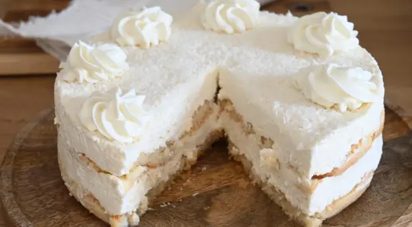 Torta soffice con strati di pan di Spagna e crema alla ricotta, ricoperta di cocco grattugiato e decorata con ciuffi di panna.