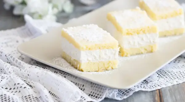 Tre soffici fette di torta Kinder Paradiso, cosparse di zucchero a velo, su un piatto bianco.