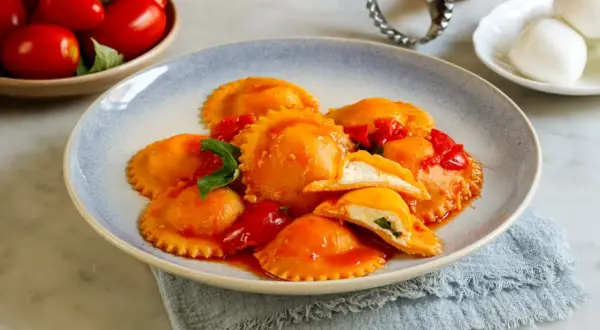 Ravioli capresi ripieni di ricotta e basilico, conditi con salsa di pomodoro fresco e guarniti con foglie di basilico.