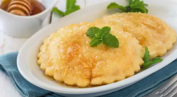 Seadas ricetta: dolci fritti dorati, guarniti con miele e menta fresca, su un piatto bianco.