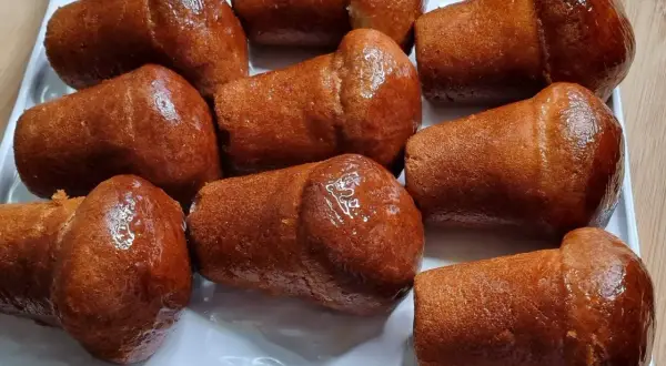 Un vassoio bianco pieno di deliziosi babà dorati, inzuppati in uno sciroppo lucido.