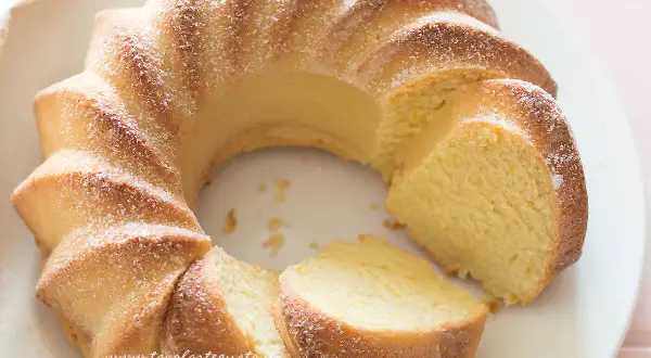 Una soffice torta di ricotta, spolverata di zucchero a velo, tagliata a fette su un piatto bianco.