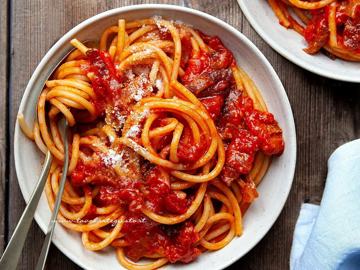 Un piatto di bucatini all'amatriciana ricetta, conditi con sugo rosso e guanciale croccante, spolverati di pecorino.