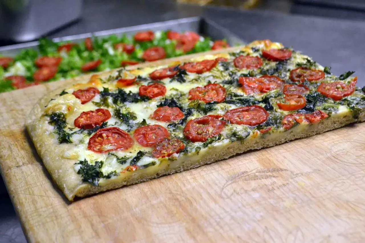 Focaccia messinese con pomodorini e verdure, un sapore autentico su un tagliere di legno.