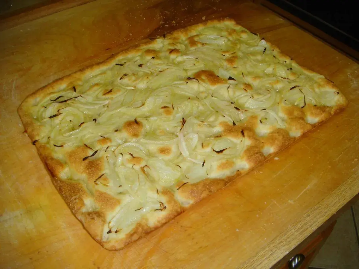 Focaccia con cipolle appena sfornata, dorata e fragrante, adagiata su un tagliere di legno.