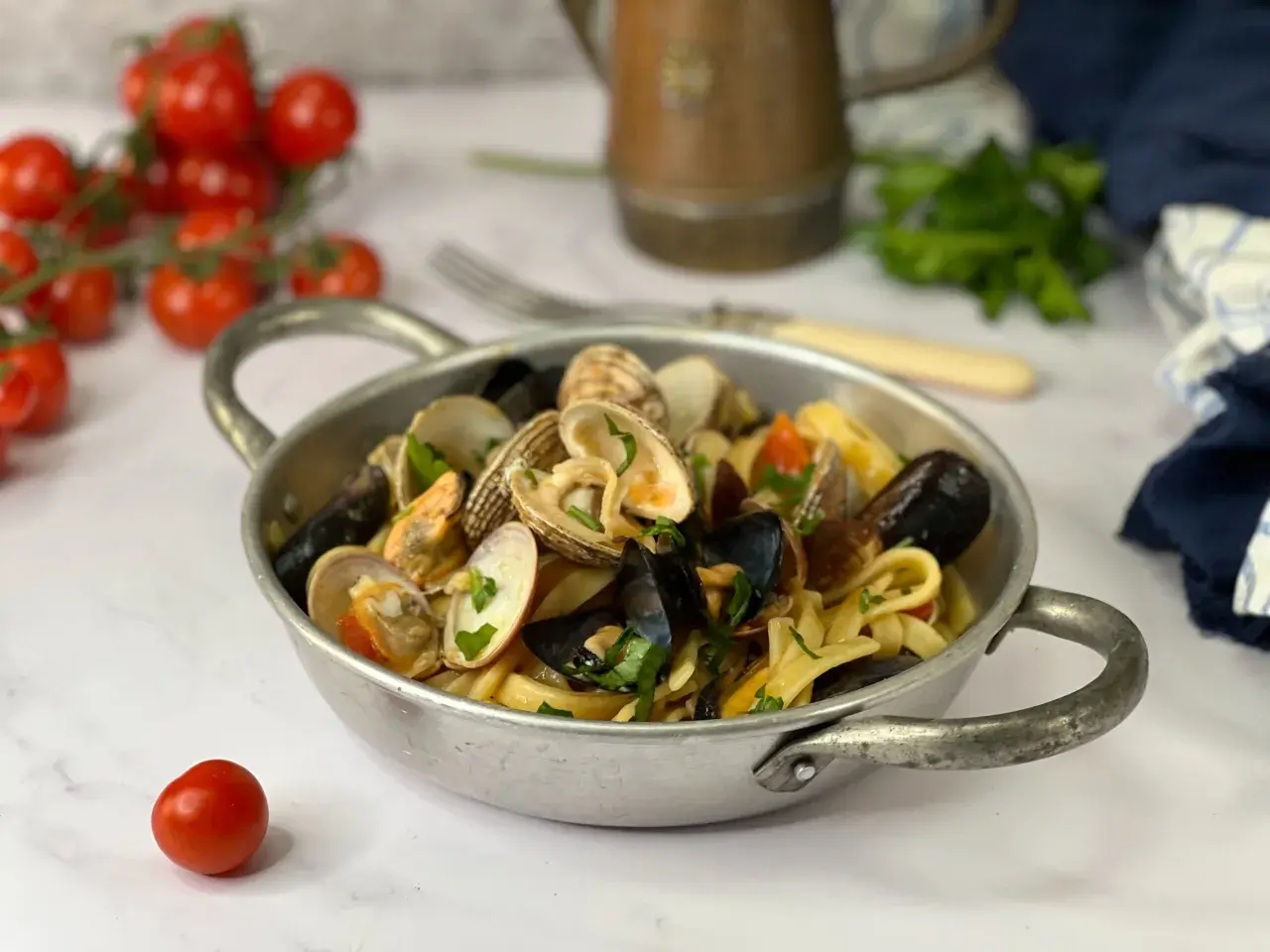 Un piatto di scialatielli ai frutti di mare, con cozze, vongole e pomodorini, guarnito con prezzemolo fresco.