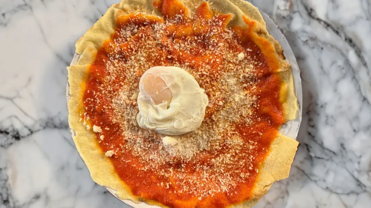 Piatto con pane carasau, salsa di pomodoro, formaggio grattugiato e uovo in camicia. Un'idea per gustose ricette.