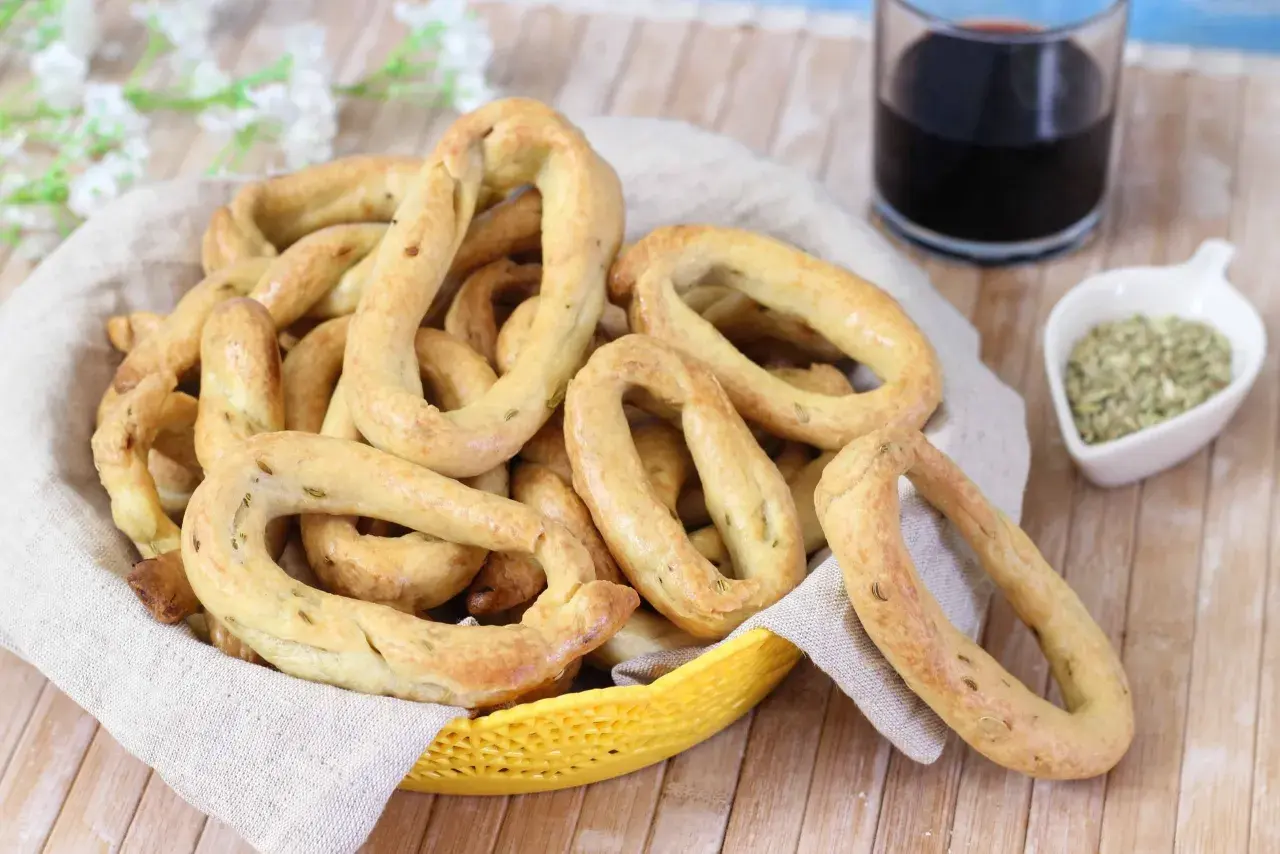 Taralli al finocchietto con lievito, croccanti e profumati, in un cestino con un bicchiere di vino rosso e semi di finocchio.