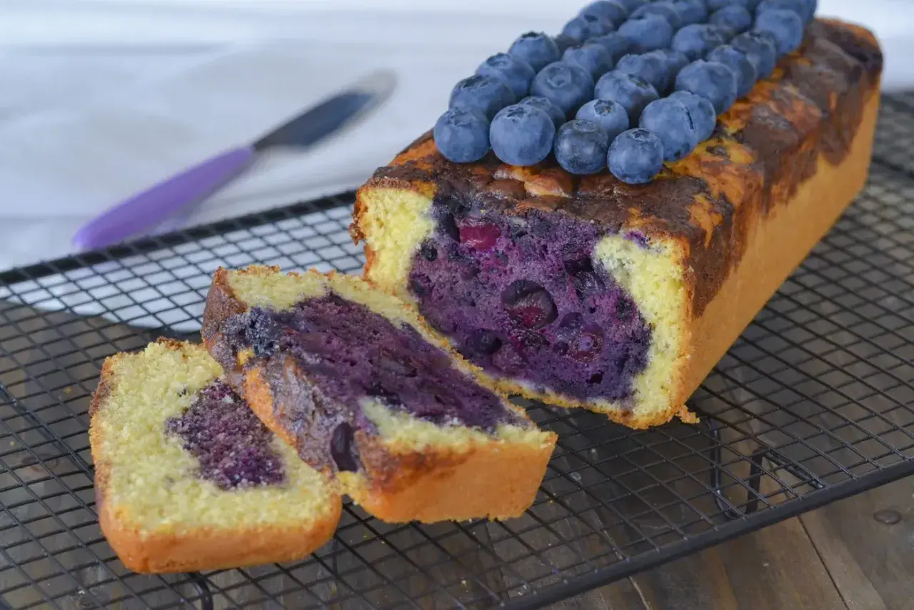 Plumcake ai mirtilli appena sfornato, con mirtilli freschi in cima e all'interno, su una griglia di raffreddamento.
