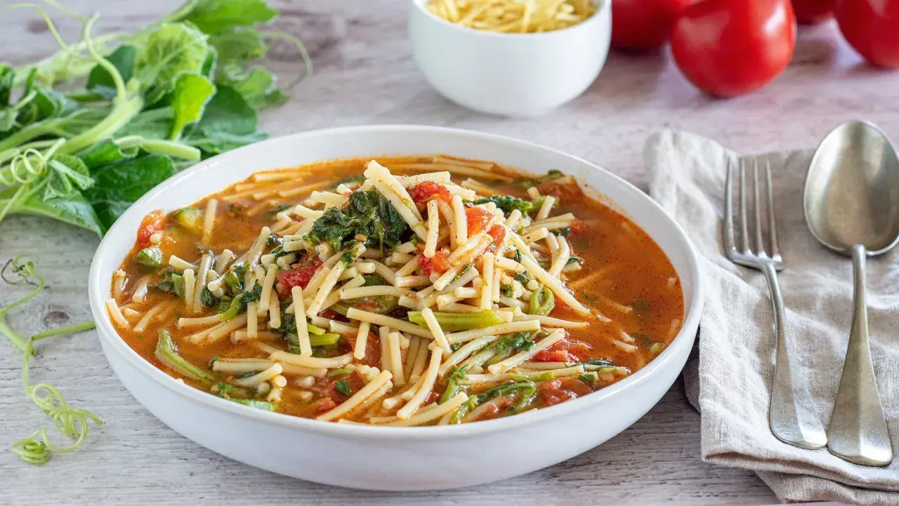 Piatto di pasta con i tenerumi asciutta, pomodoro e verdure fresche, pronto per essere gustato.