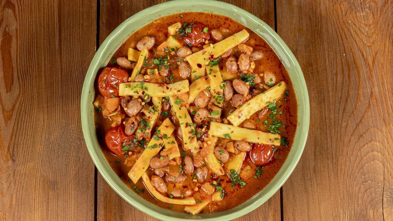 Piatto di sagne e fagioli fumante, con pomodorini e prezzemolo tritato, servito in una ciotola verde su un tavolo di legno.