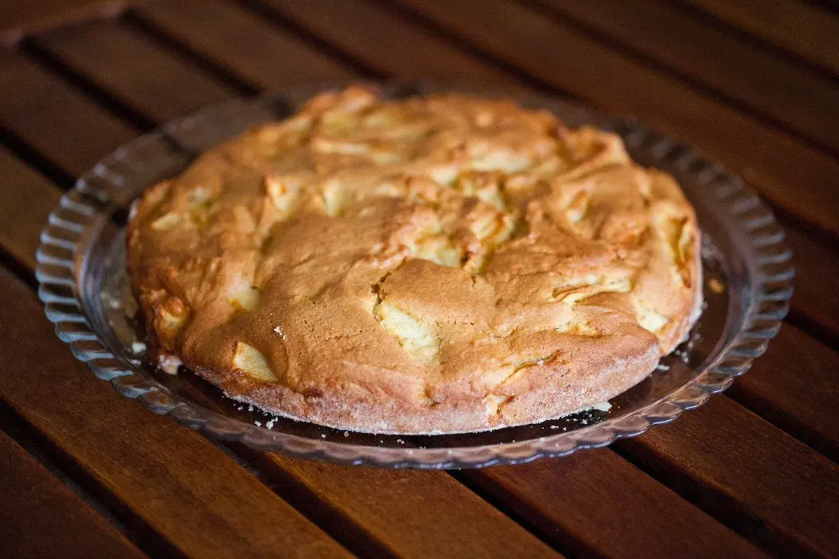 Torta di pane e mele alla trentina, dorata e invitante, su un piatto di vetro, pronta per essere gustata.