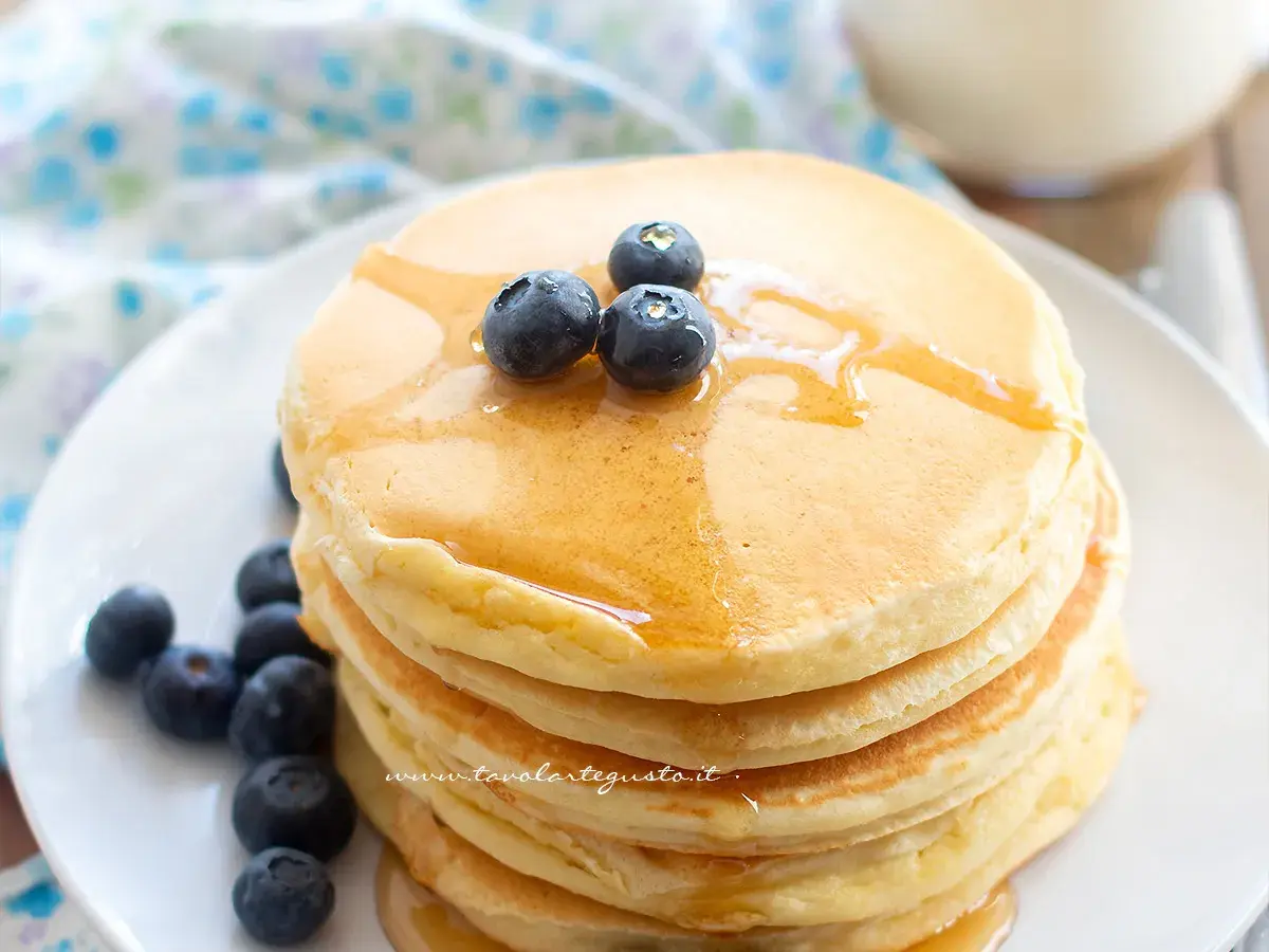 Pancakes senza glutine dorati, impilati e guarniti con mirtilli freschi e sciroppo d'acero.