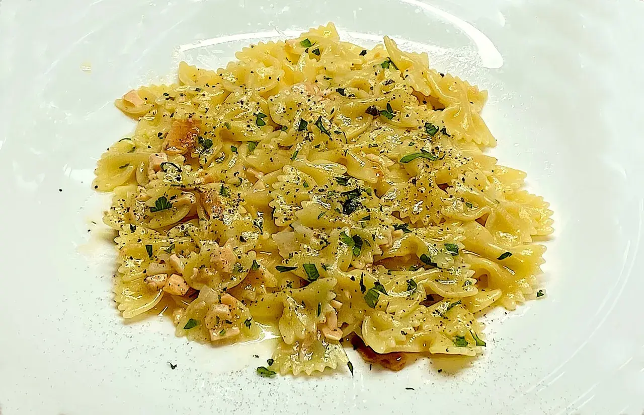 Farfalle condite con cubetti di salmone rosa, prezzemolo tritato e pepe nero. Un piatto di pasta al salmone invitante.
