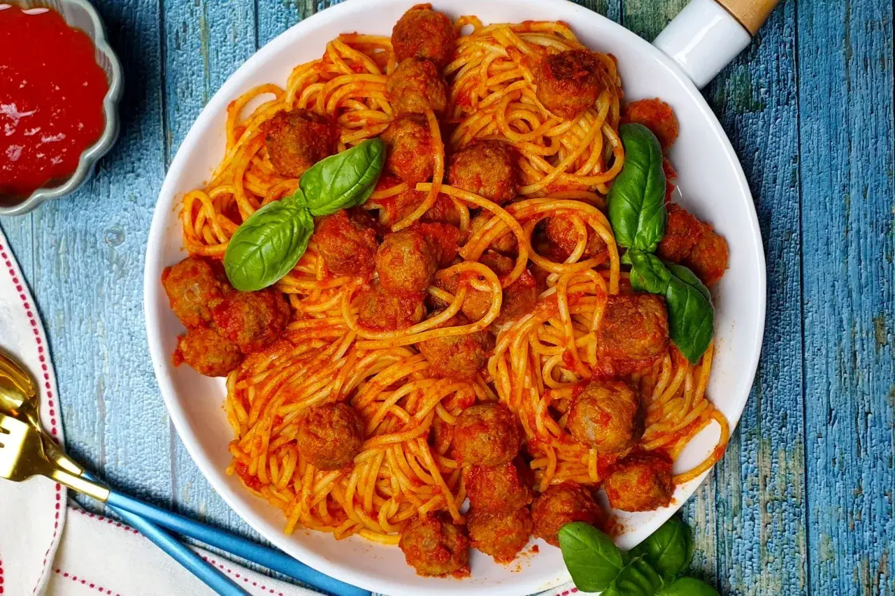 Un piatto invitante di spaghetti con polpette, conditi con salsa rossa e guarniti con foglie di basilico fresco.