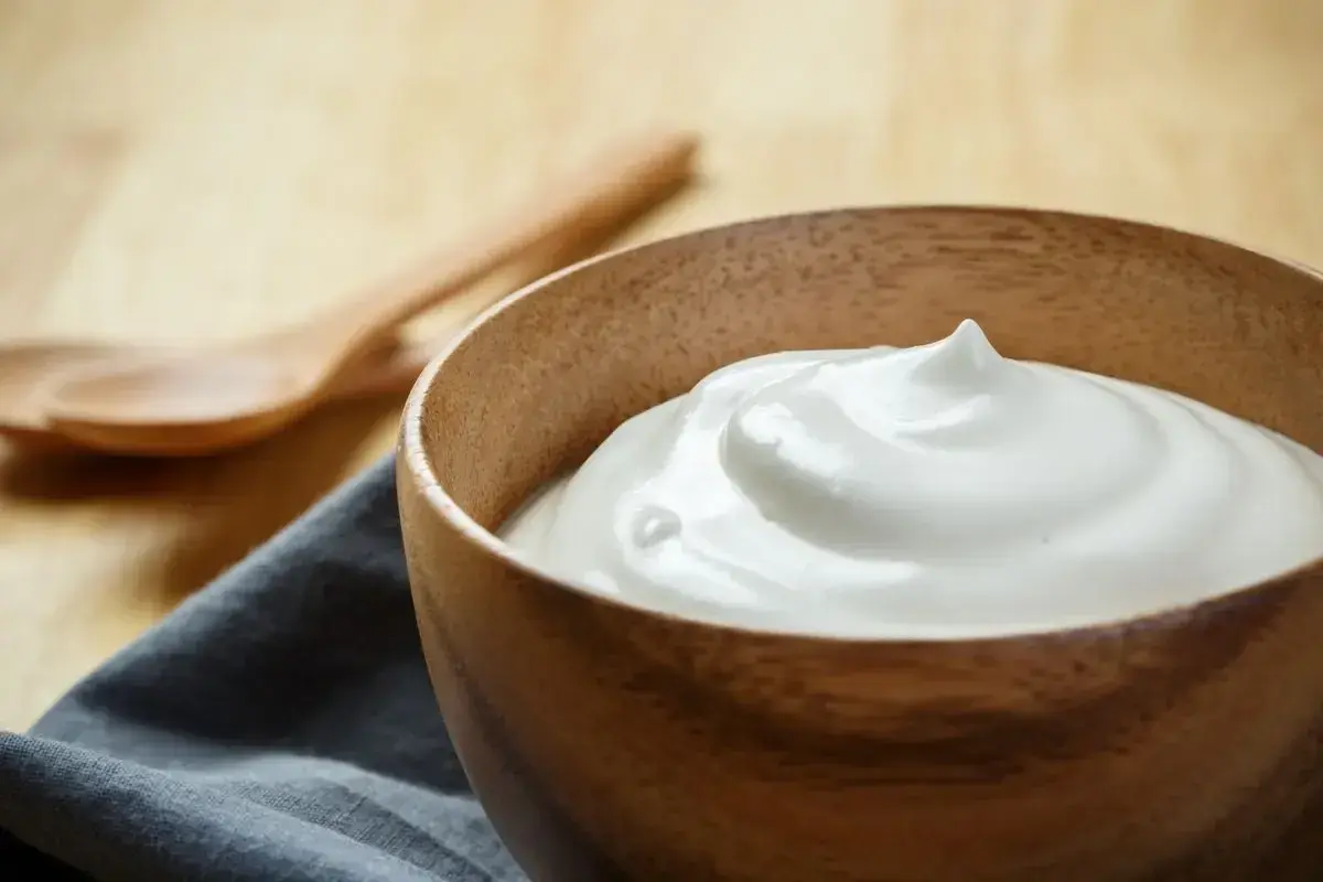 Una ciotola di legno piena di soffice crema di latte, perfetta per la tua prossima ricetta. Due cucchiai di legno sullo sfondo.