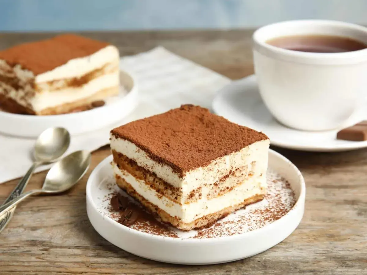 Delizioso tiramisù, perfetto per la tua tiramisù ricetta benedetta. Servito su un piatto bianco con caffè e cucchiaini.