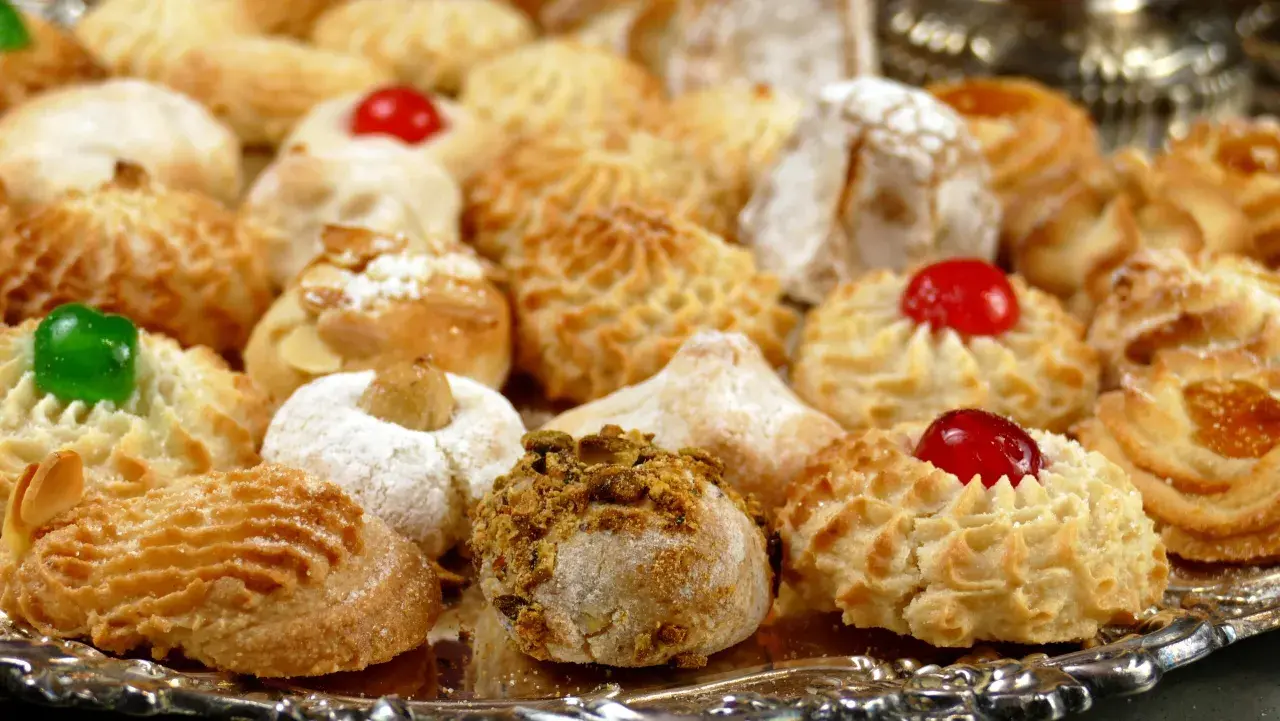 Vassoio pieno di dolcetti invitanti, tra cui spiccano le paste di mandorla decorate con ciliegie candite e granella di pistacchio.