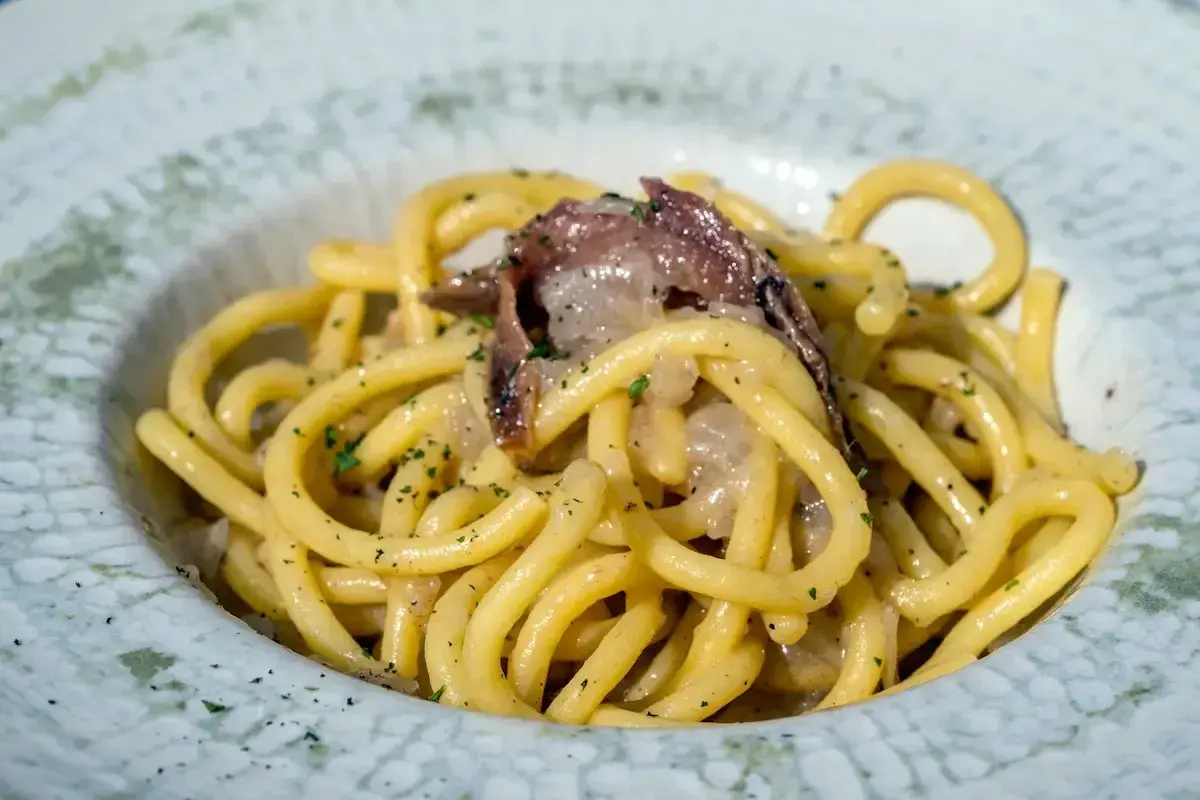 Un piatto di bigoli in salsa, con pasta spessa e condimento saporito, guarnito con prezzemolo tritato.