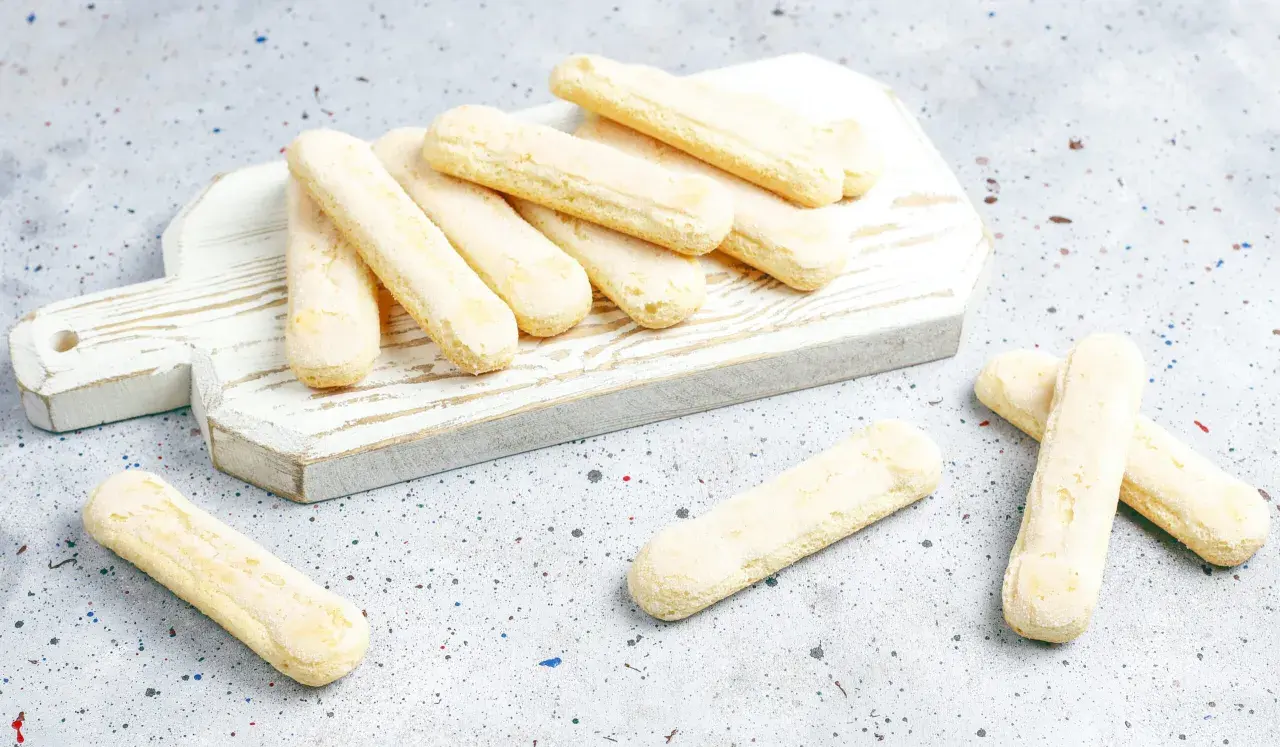 Savoiardi pronti per la ricetta del tiramisù, disposti su un tagliere bianco.