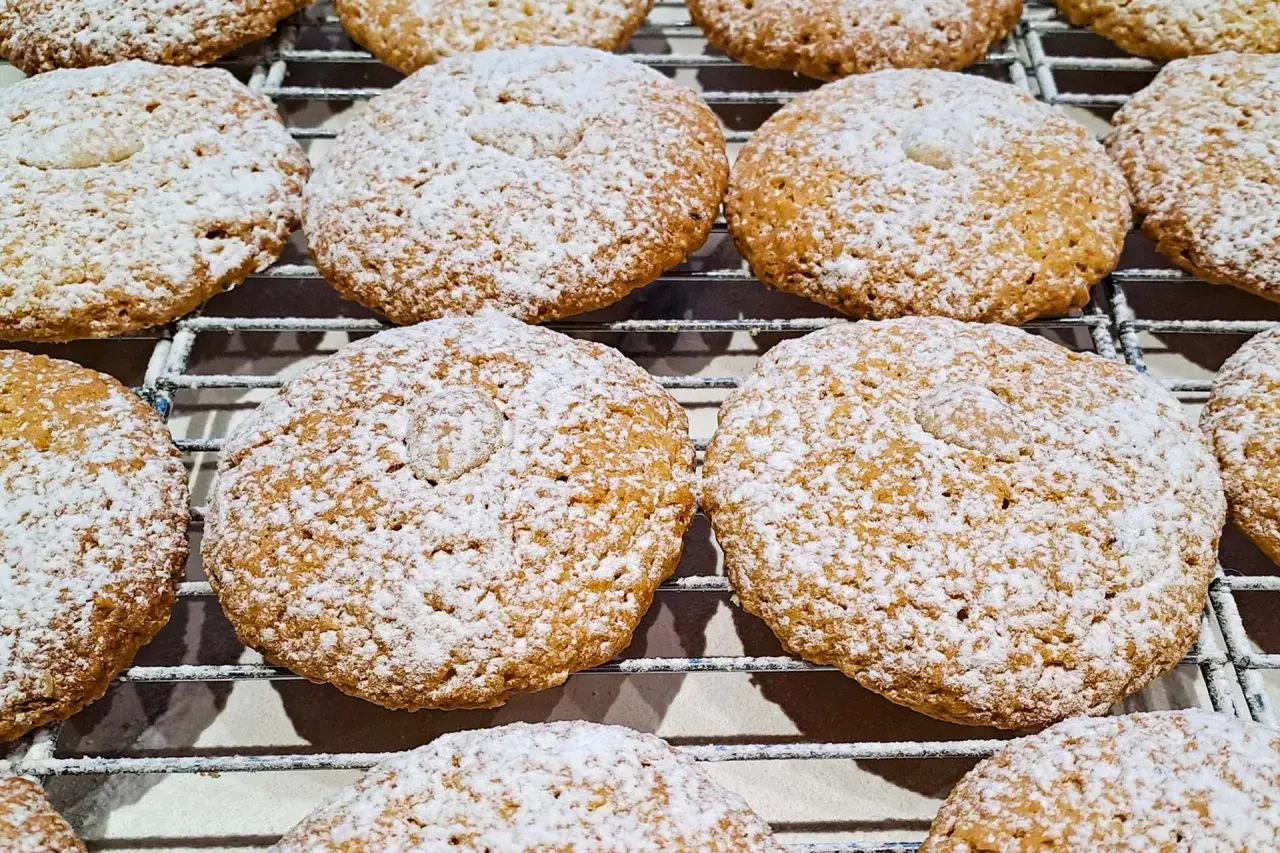 Biscotti con farina di mandorle, cosparsi di zucchero a velo, riposano su una griglia.
