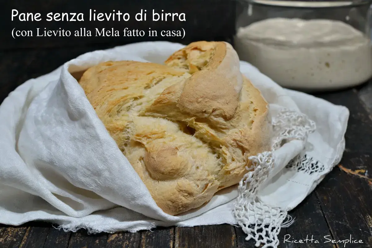 Pane senza lievito di birra, dorato e fragrante, avvolto in un panno bianco. Accanto, un vasetto con lievito madre alla mela.
