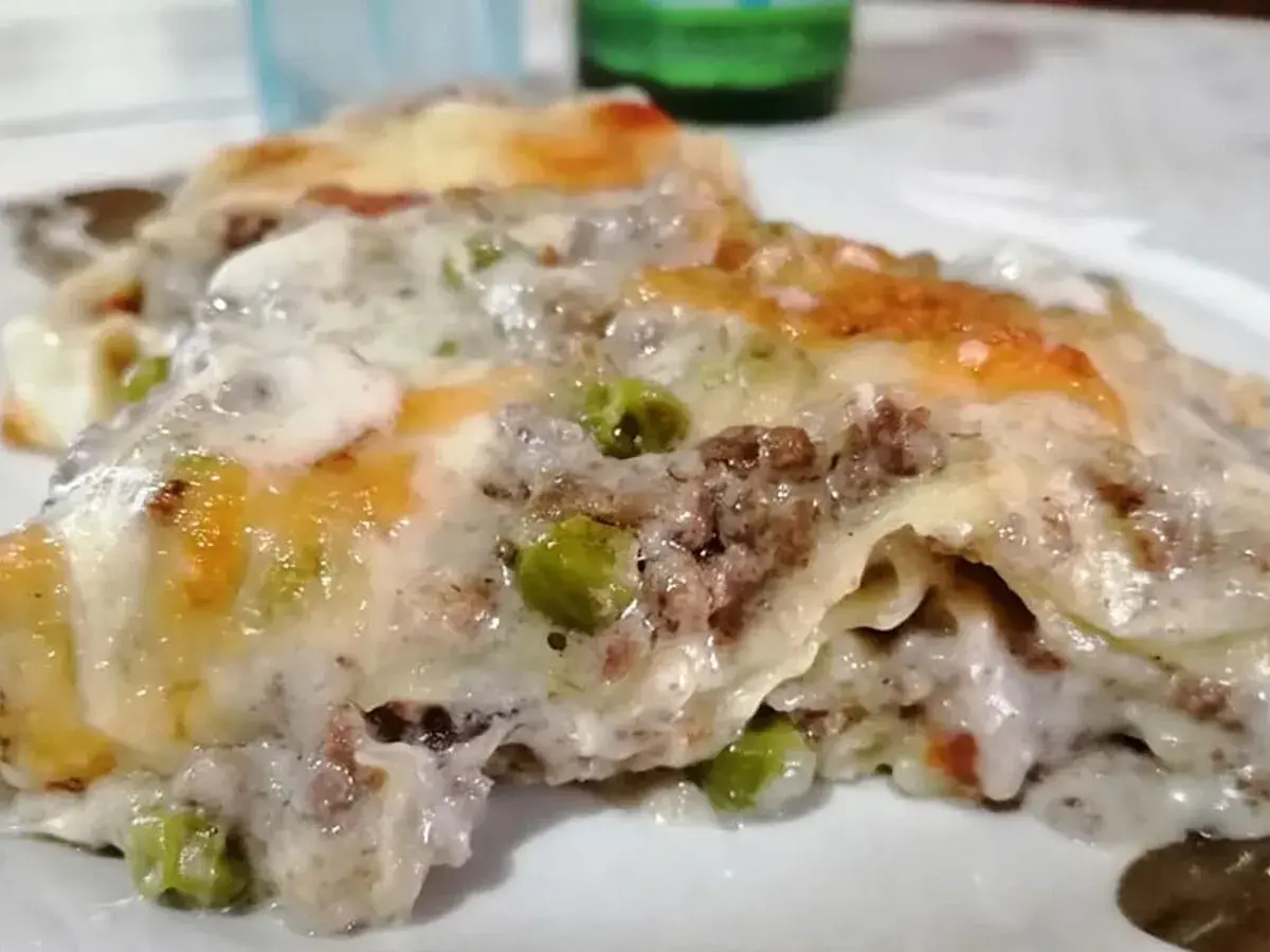 Porzione di lasagna bianca con ragù, piselli e besciamella filante, gratinata al forno.