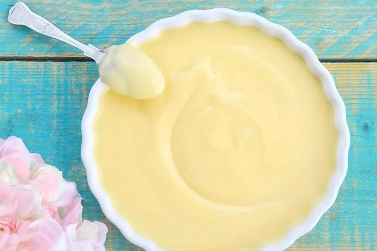 Crema pasticcera ricetta della nonna, liscia e vellutata, pronta per essere gustata. Un cucchiaio d'argento ne assapora la bontà.