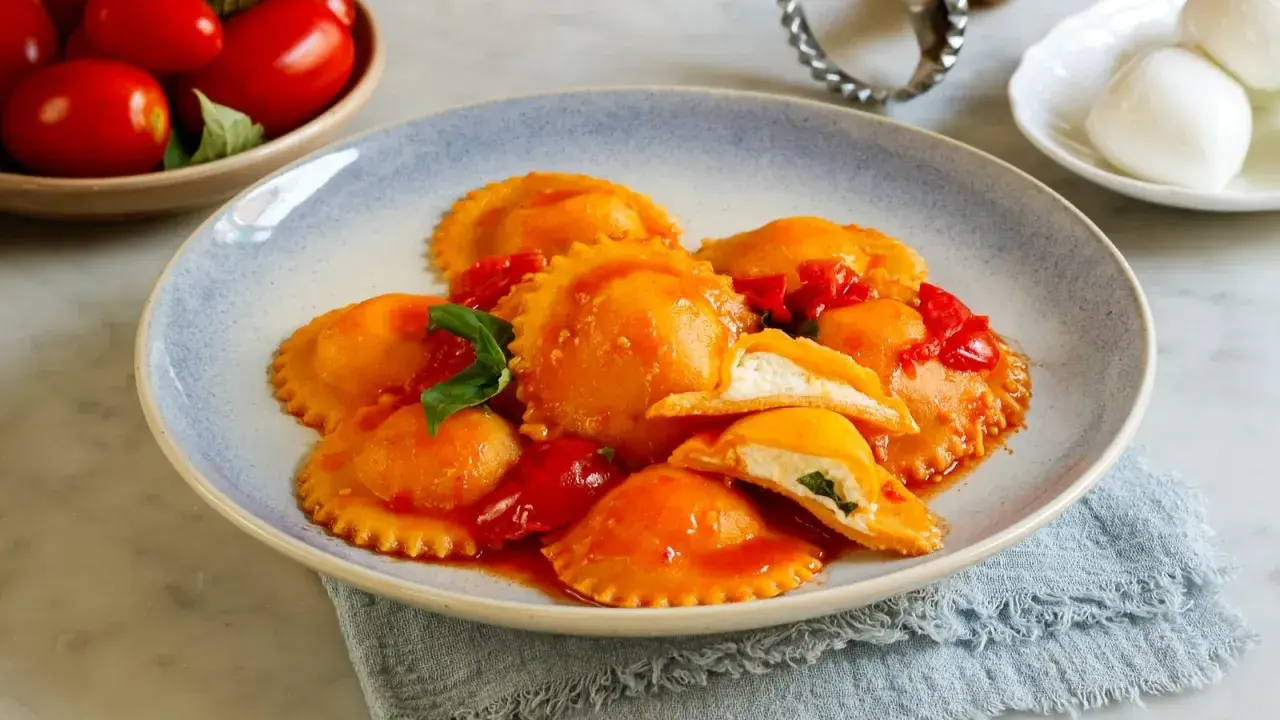 Ravioli capresi ripieni di ricotta e basilico, conditi con salsa di pomodoro fresco e guarniti con foglie di basilico.