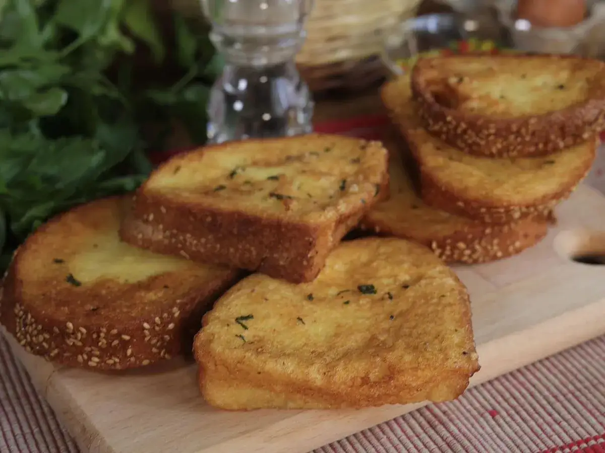 Fette dorate di pane fritto, cosparse di semi di sesamo e erbe aromatiche, pronte per essere gustate.