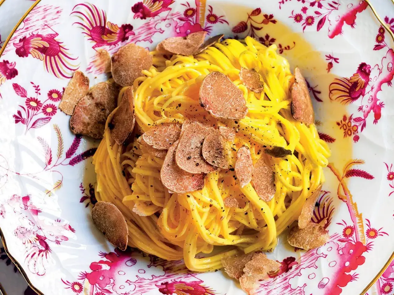 Un piatto di tagliolini al tartufo, conditi con una salsa cremosa e generose scaglie di tartufo fresco, serviti su un elegante piatto decorato con motivi floreali e uccelli.