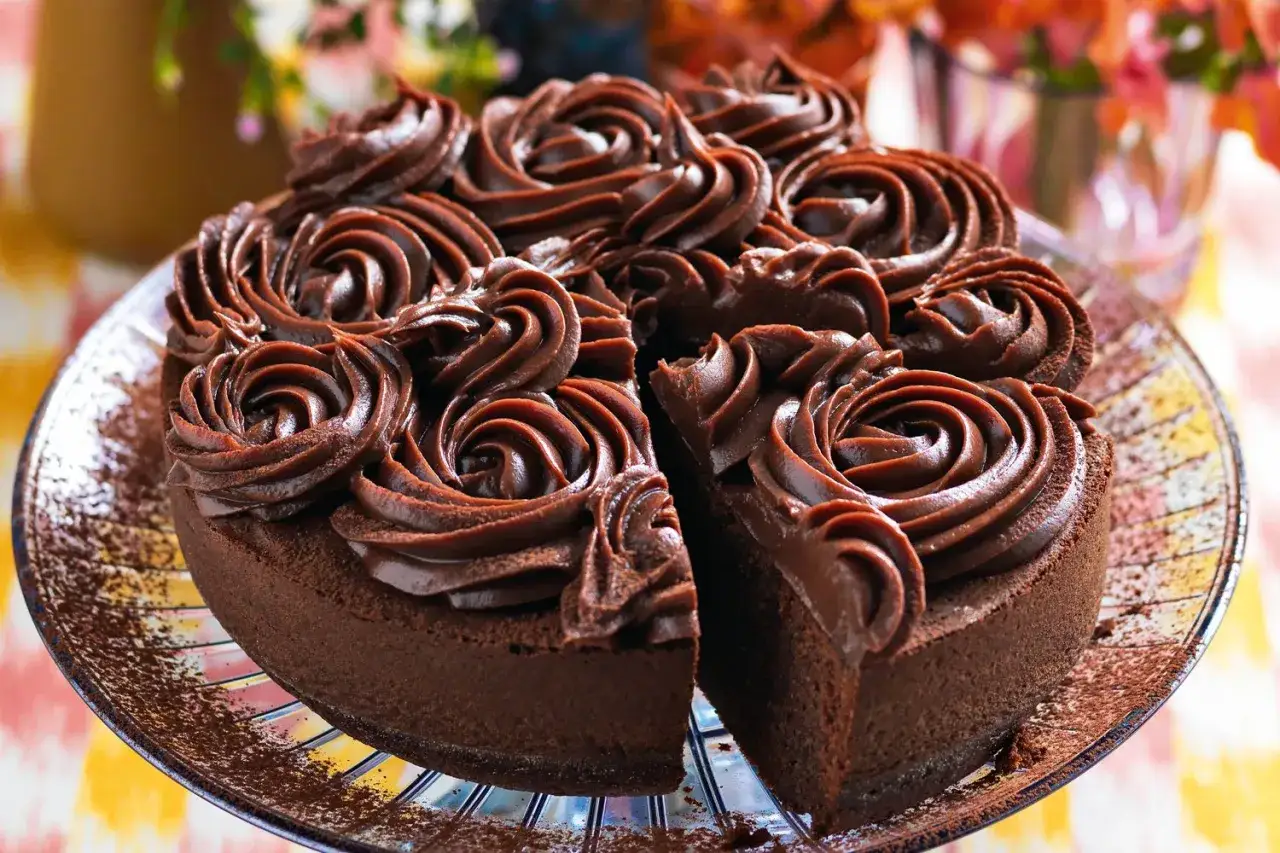 Torta al cioccolato con decorazioni a rosa realizzate con ganache cioccolato per copertura. Una fetta è stata rimossa, rivelando la morbidezza interna.