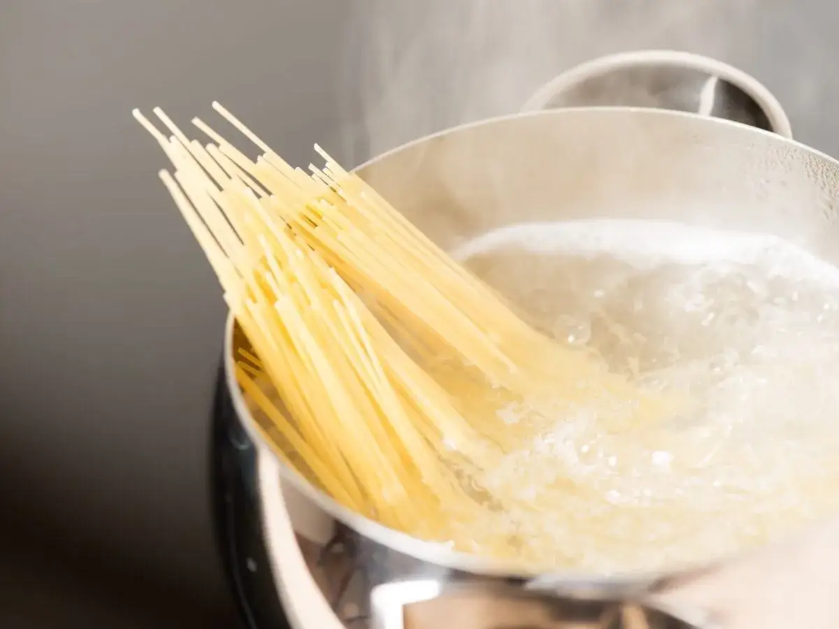 Spaghetti crudi immersi in acqua bollente, pronti per imparare come cucinare la pasta perfetta.