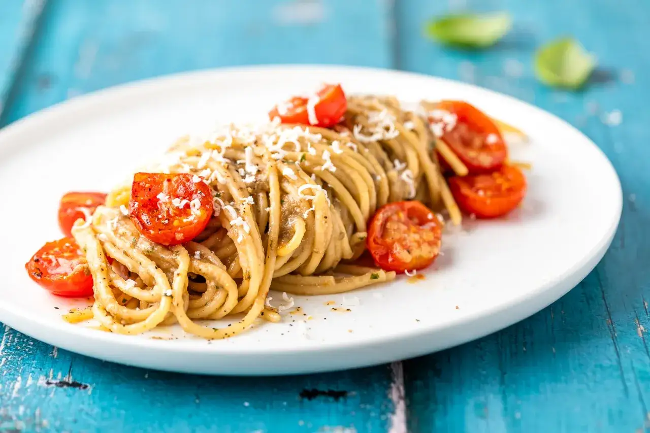 Spaghetti conditi con una deliziosa crema di melanzane per pasta, guarniti con pomodorini confit e parmigiano grattugiato.