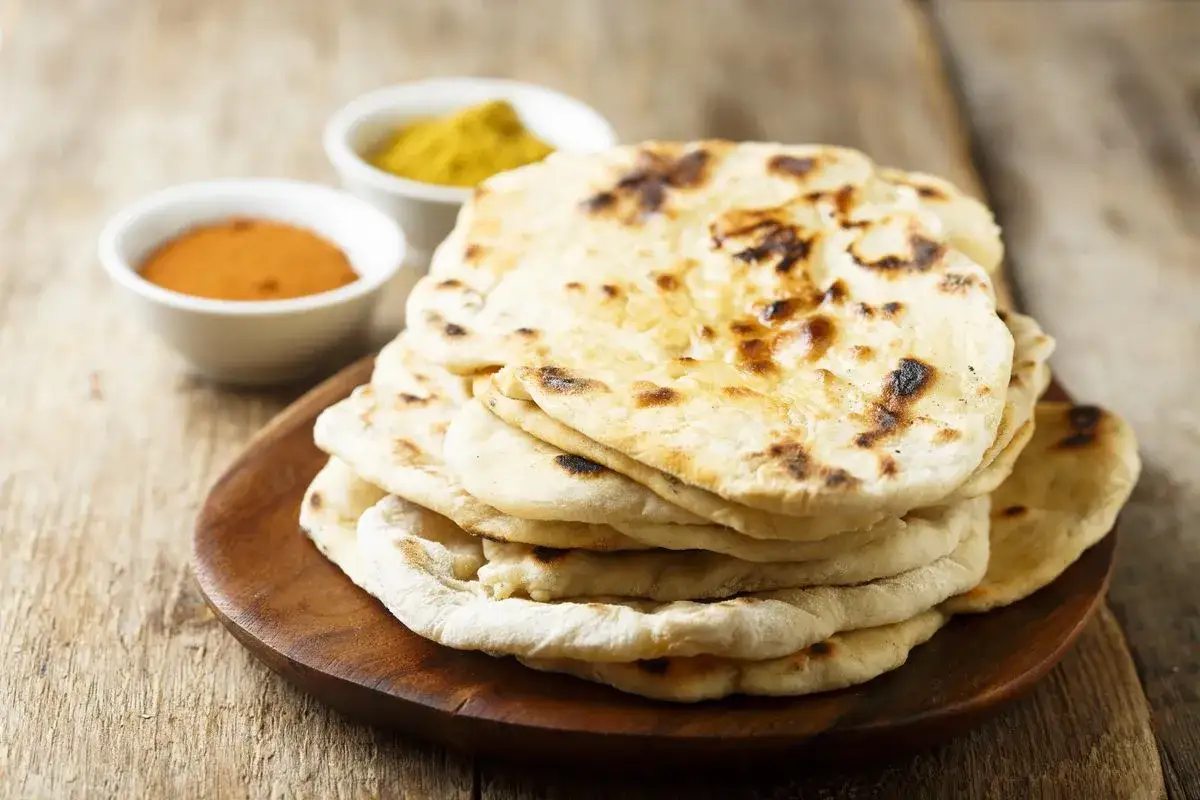 Una pila di pane naan appena sfornato, con due ciotoline di spezie in sottofondo.