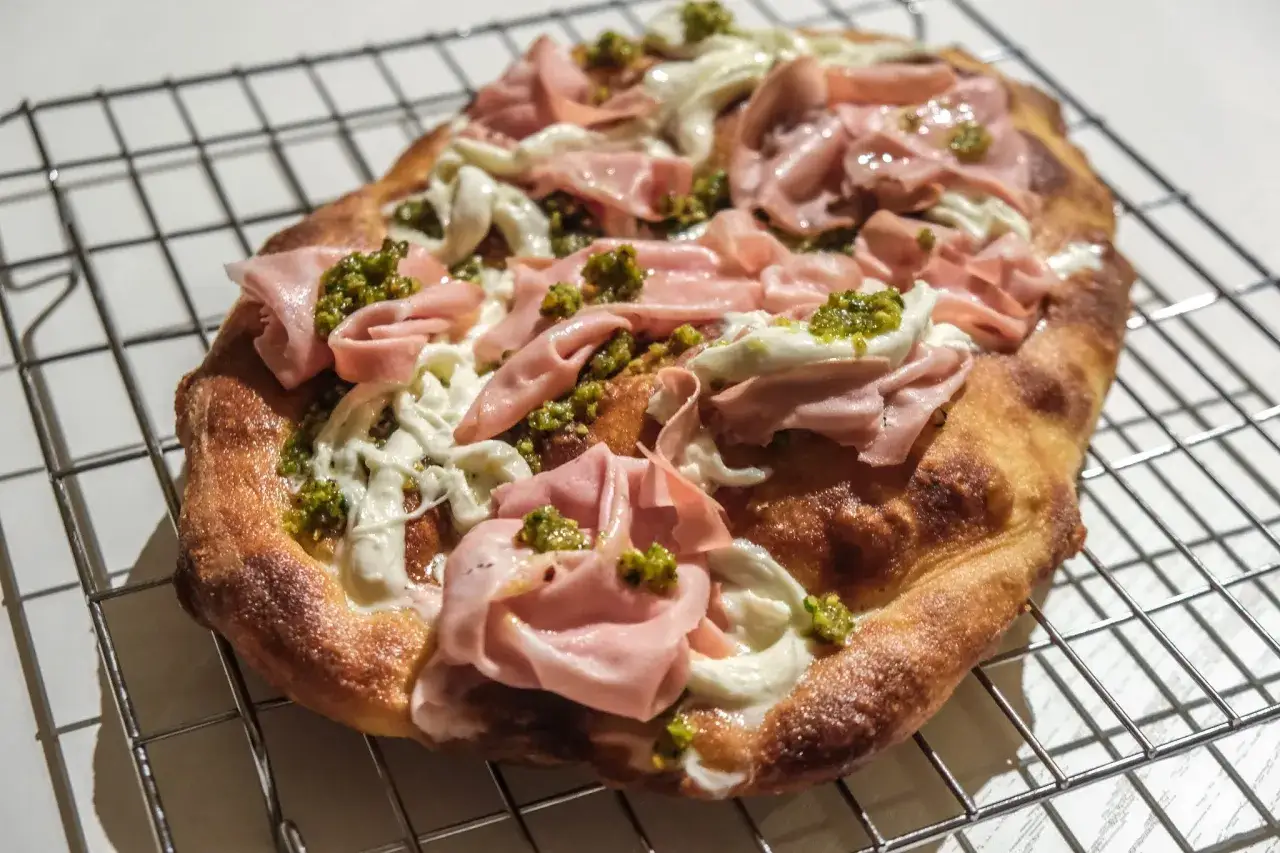 Pizza con mortadella, mozzarella filante e pesto di pistacchio su griglia.